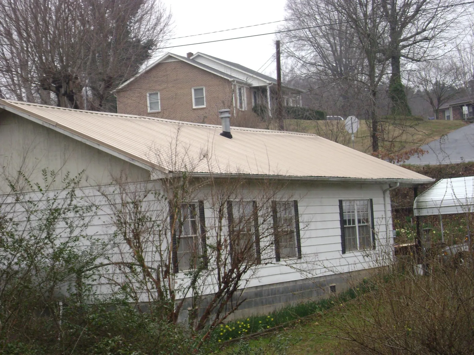 Tan metal roof on a white sided house set into a hillside — Commercial Roofing by Roofing Brothers in Cambridge